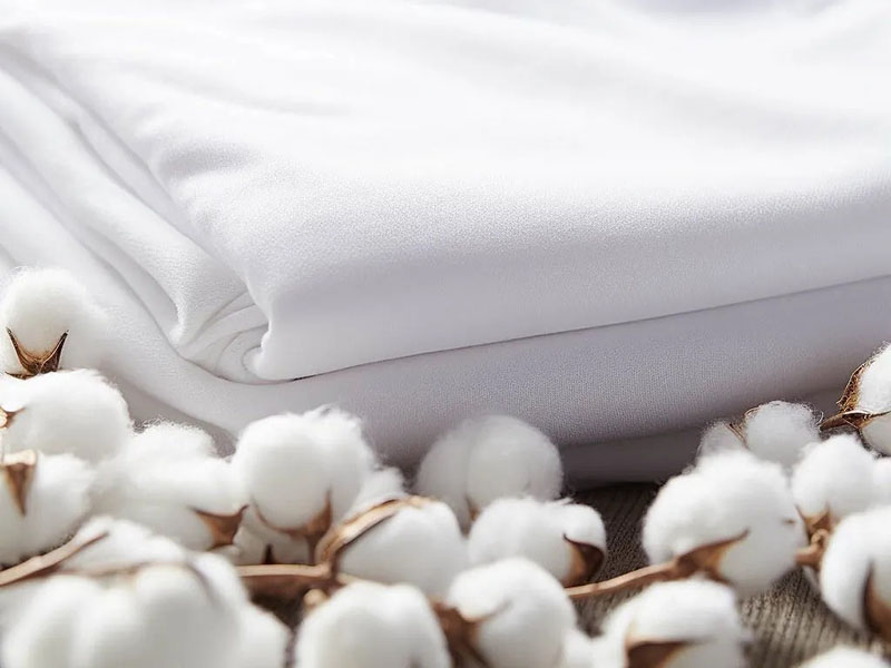 Folded white fabric with cotton bolls arranged on wooden surface