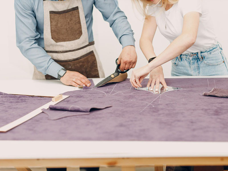 Two designers cutting purple fabric pattern pieces on worktable