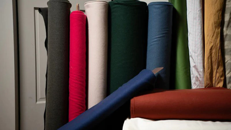 Several large rolls of fabric in various colors and checked patterns, standing upright against a wall.