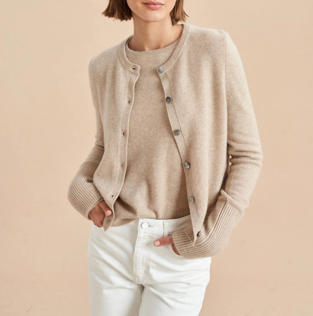 Woman wearing a beige knit cardigan set with white pants against a neutral background.