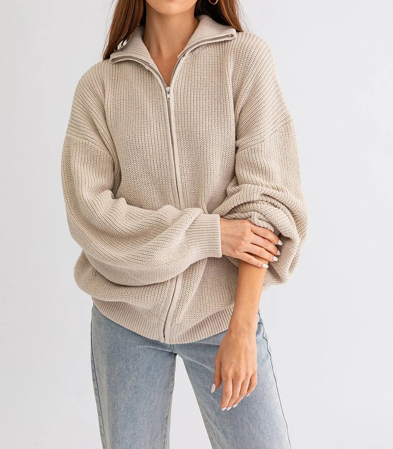 Woman wearing beige zip-up knit cardigan with relaxed sleeves and light jeans