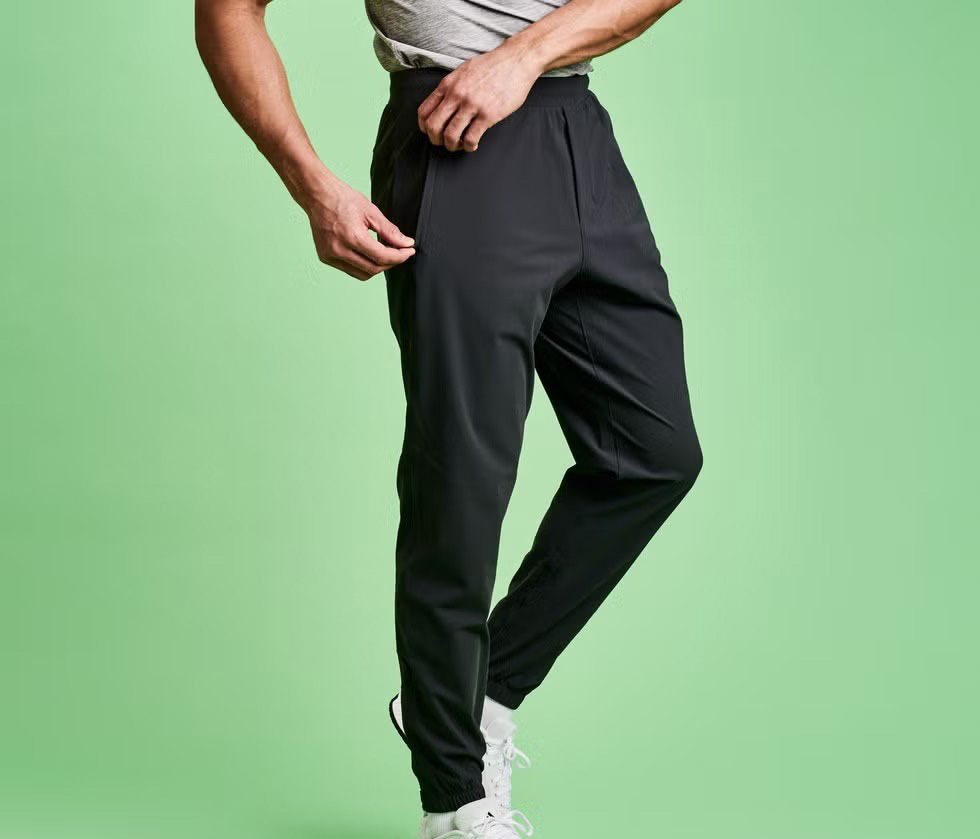 Man wearing slim black joggers with tapered cuffs against green background