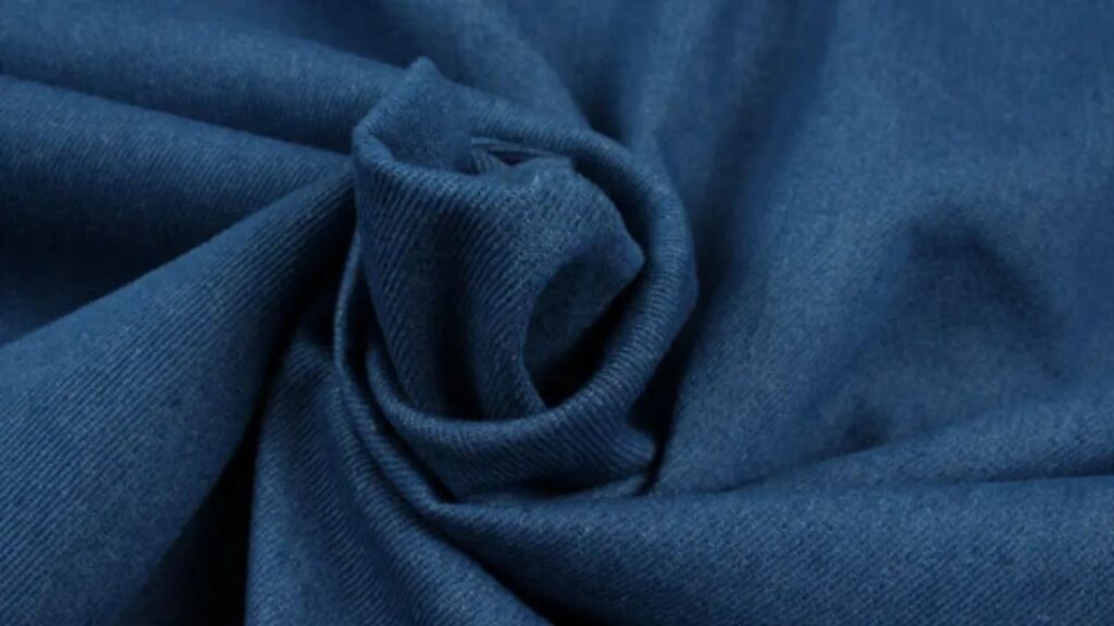Close-up of blue knit fabric twisted to show soft texture and drape.