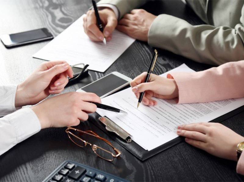 Professionals signing and reviewing documents at meeting table with phones, calculator, and clipboard