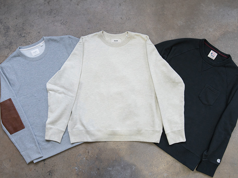 Three crewneck sweatshirts laid flat in light blue, cream, and black.