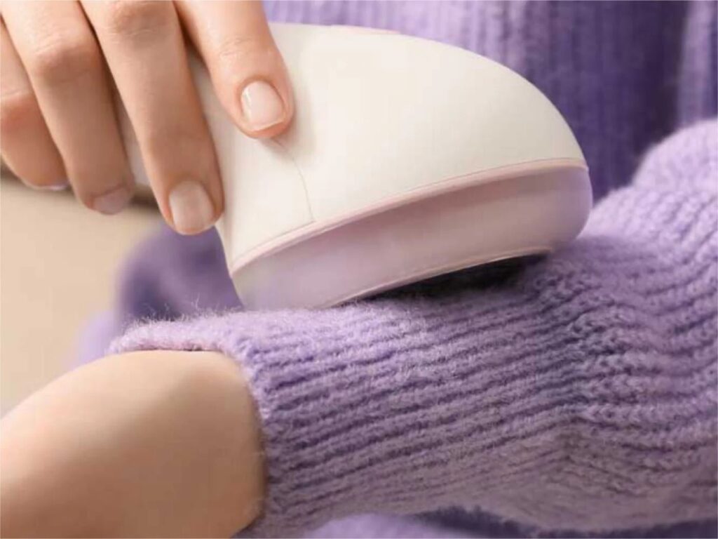 Hand using electric fabric shaver to remove pills from lavender cardigan