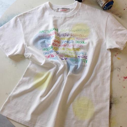 White graphic T-shirt with colorful handwritten city names laid flat