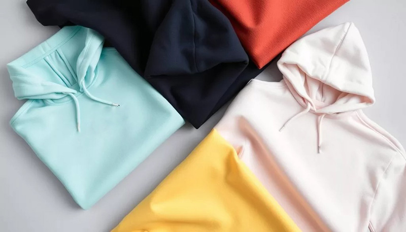 Folded hoodies in pastel and bold colors arranged neatly on a flat background.