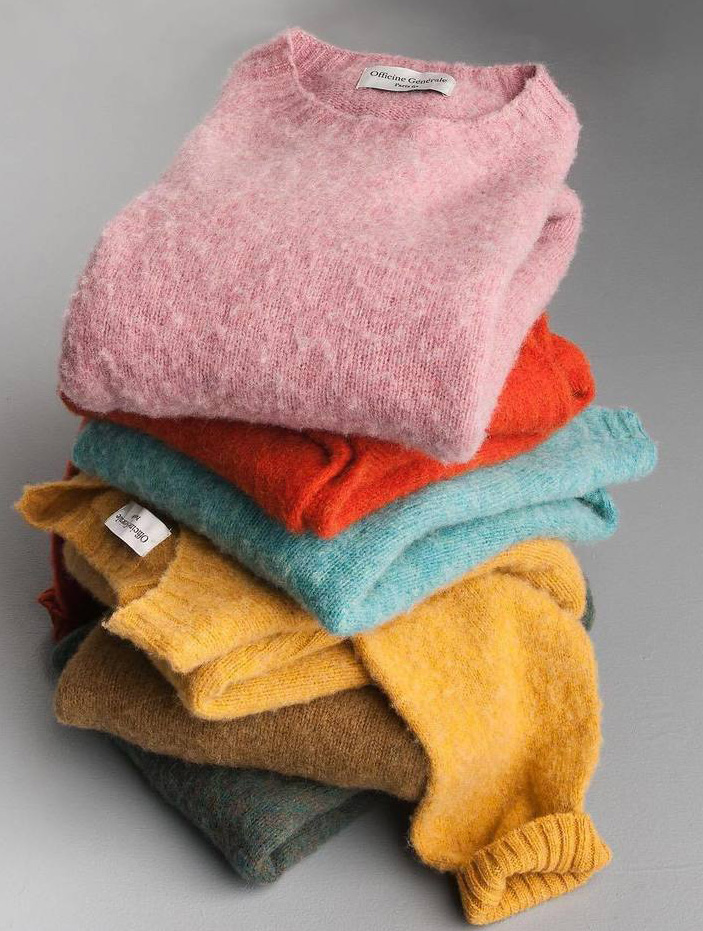 Stack of fuzzy knit sweaters in pink, orange, blue, yellow, and brown tones