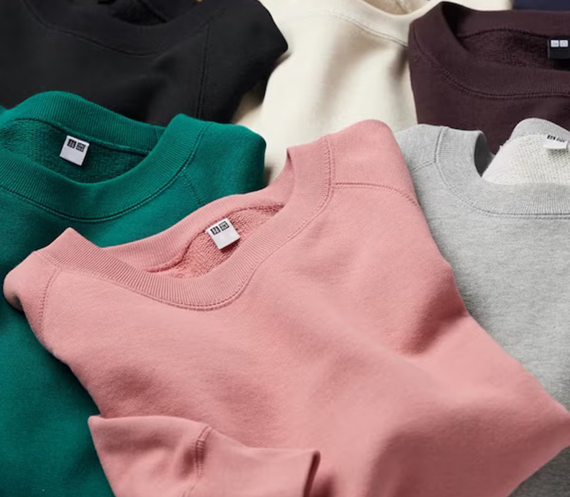 Folded crewneck sweatshirts in black, green, pink, gray, cream, and brown