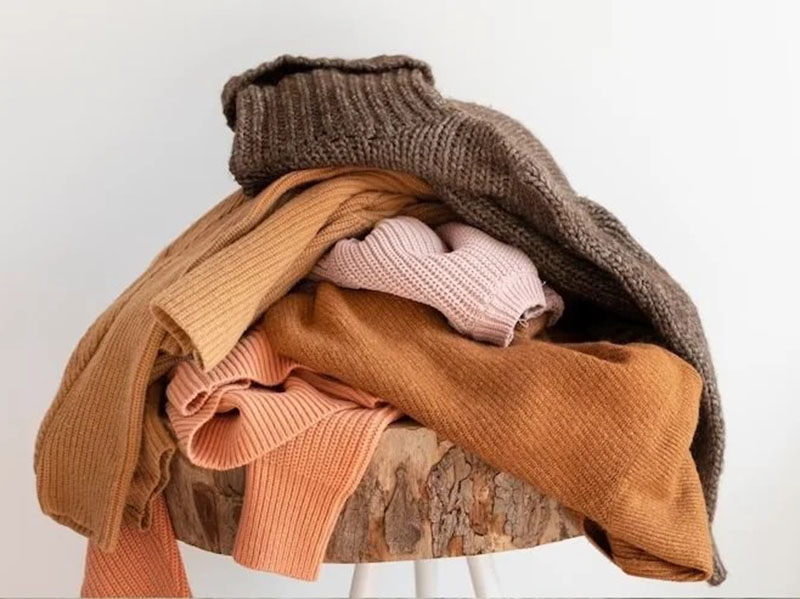 Pile of folded ribbed knit sweaters in warm neutral tones on stool