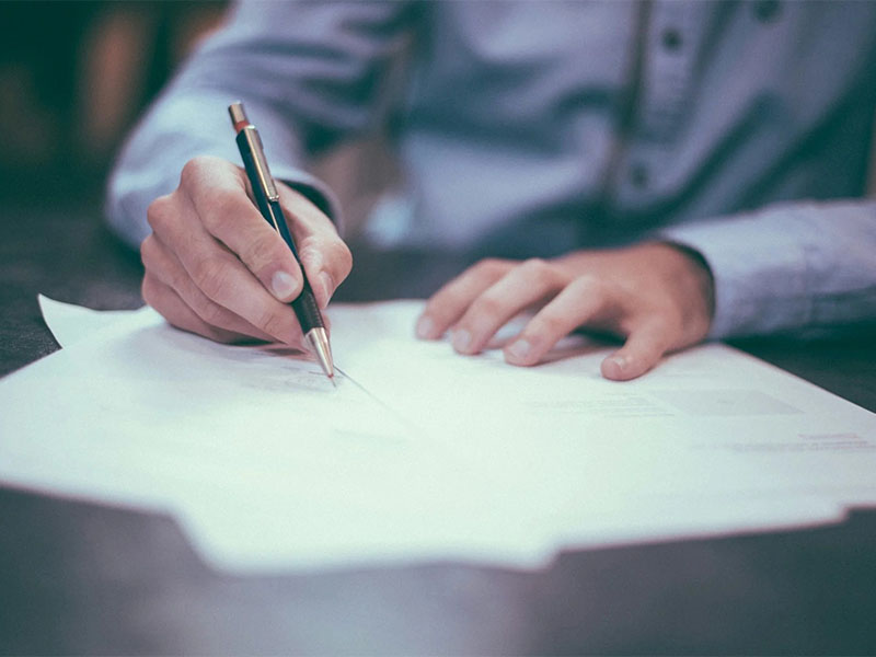 Person signing a document with pen on desk in office setting