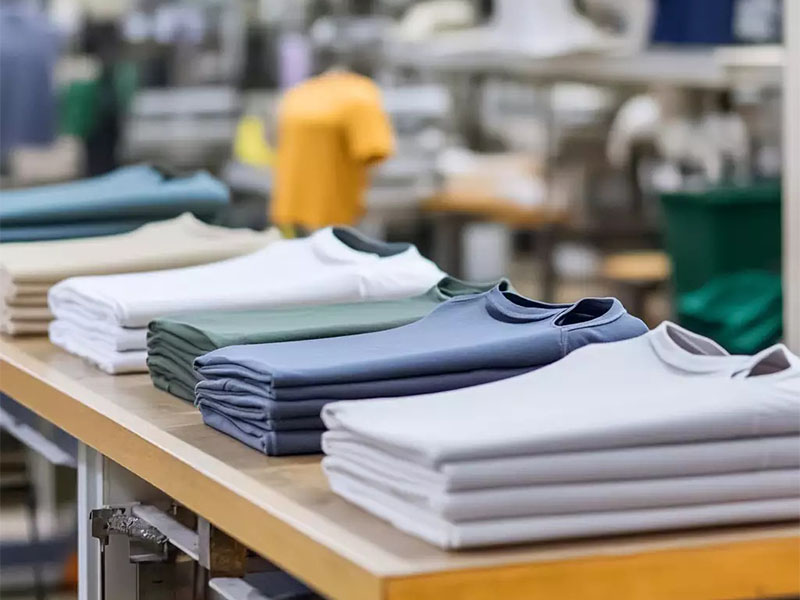 Folded plain T-shirts in soft colors arranged on worktable in garment factory