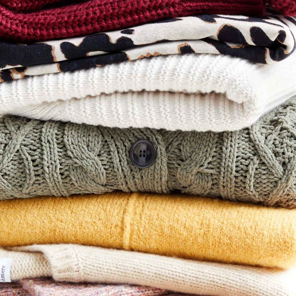 Stacked knit sweaters and cardigans in mixed textures, patterns, and warm neutral colors