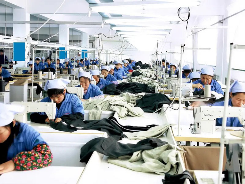 Large garment factory with workers sewing fabric along long production lines