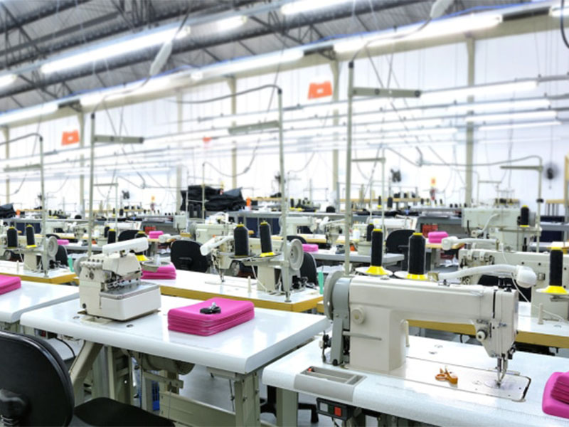 Empty garment factory floor with rows of industrial sewing machines and folded pink fabric pieces
