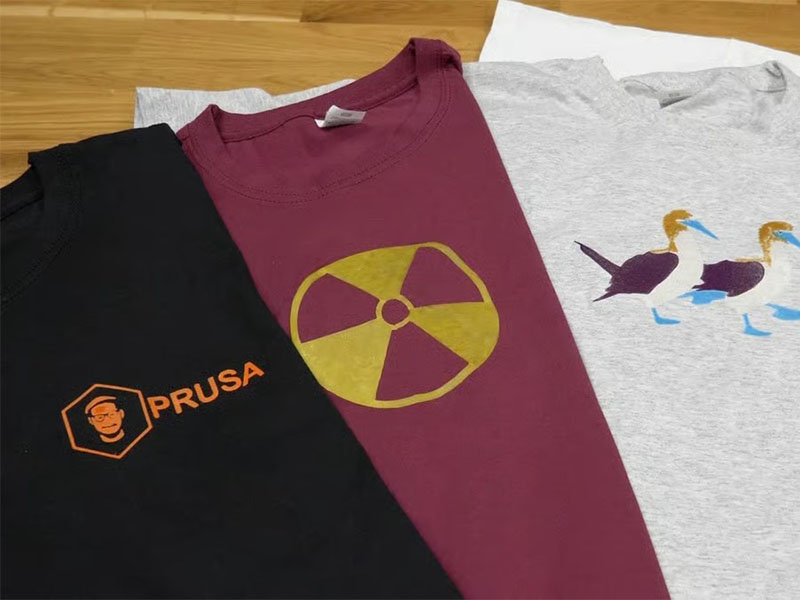 Three graphic T-shirts in black, maroon, and gray laid flat on wooden surface