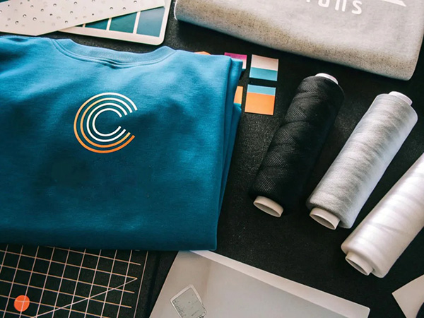 Folded blue sweatshirt with logo beside thread spools, color swatches, and print design tools.