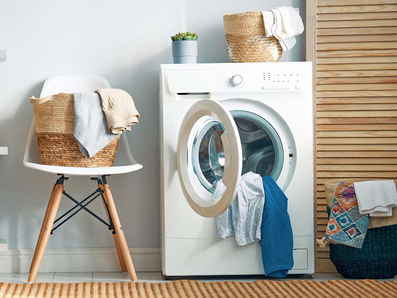 Bright laundry room with open washing machine and baskets of folded tank top