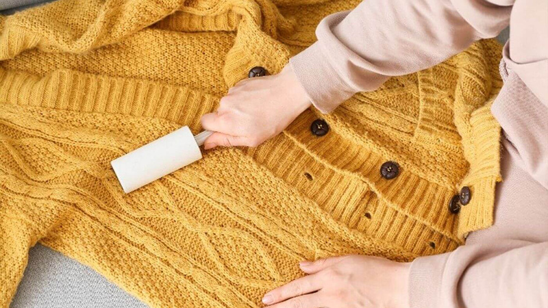 Lint roller removing fuzz from yellow cable-knit cardigan during fabric care