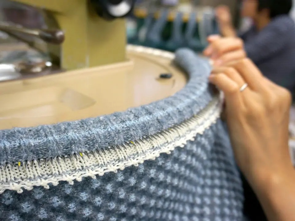 Close-up of circular knitting machine producing textured blue knit fabric