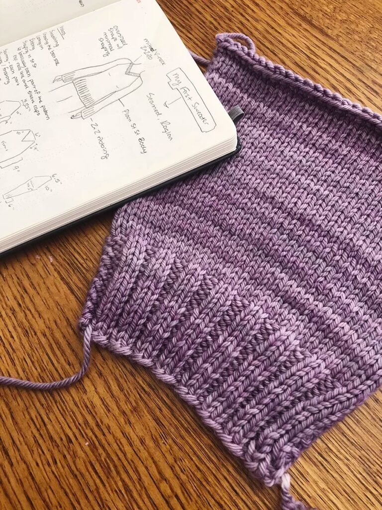 Purple knit sweater swatch beside sketchbook with handwritten garment design notes
