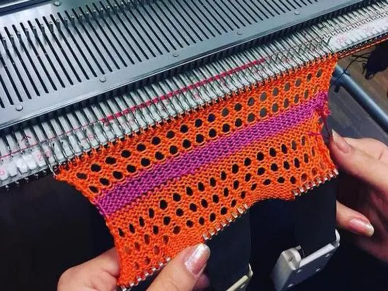 Hands operating knitting machine with orange and purple openwork fabric sample