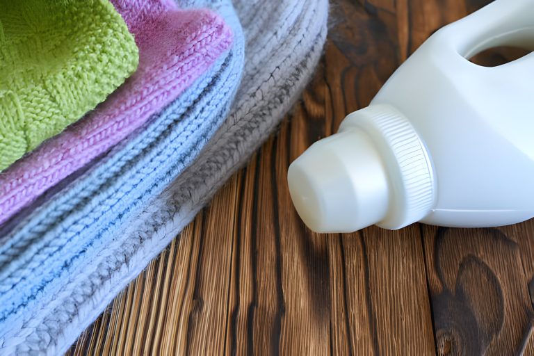 Folded colorful knit cardigan beside laundry detergent bottle on wooden surface