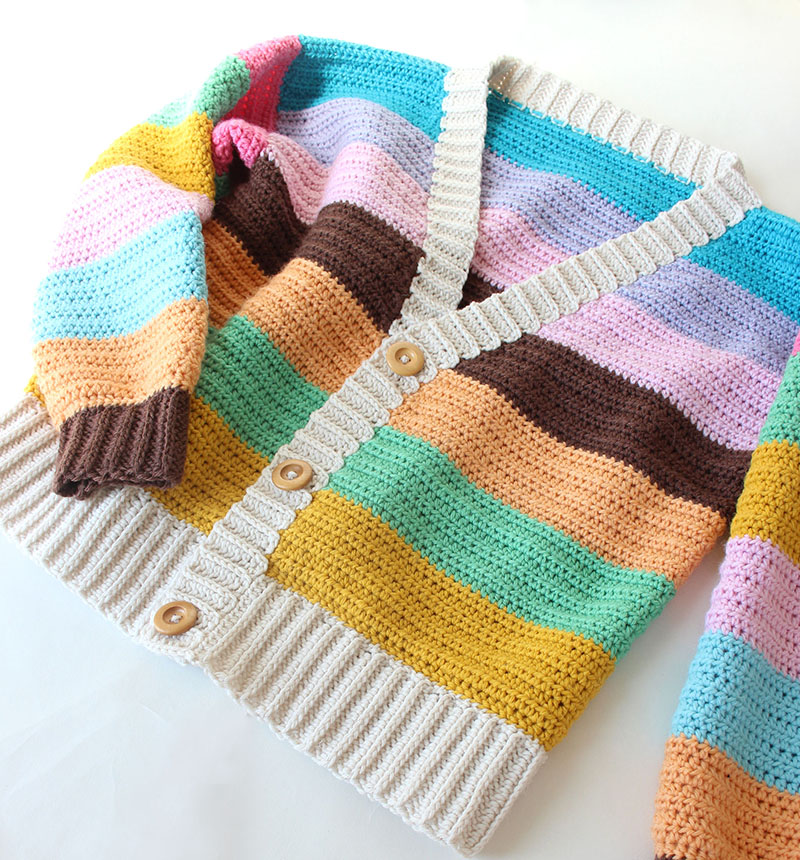 A colorful, hand-crocheted cardigan with horizontal stripes in yellow, green, brown, orange, pink, purple, and blue.