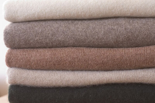 Stack of folded knit fabrics in soft neutral shades from cream to charcoal