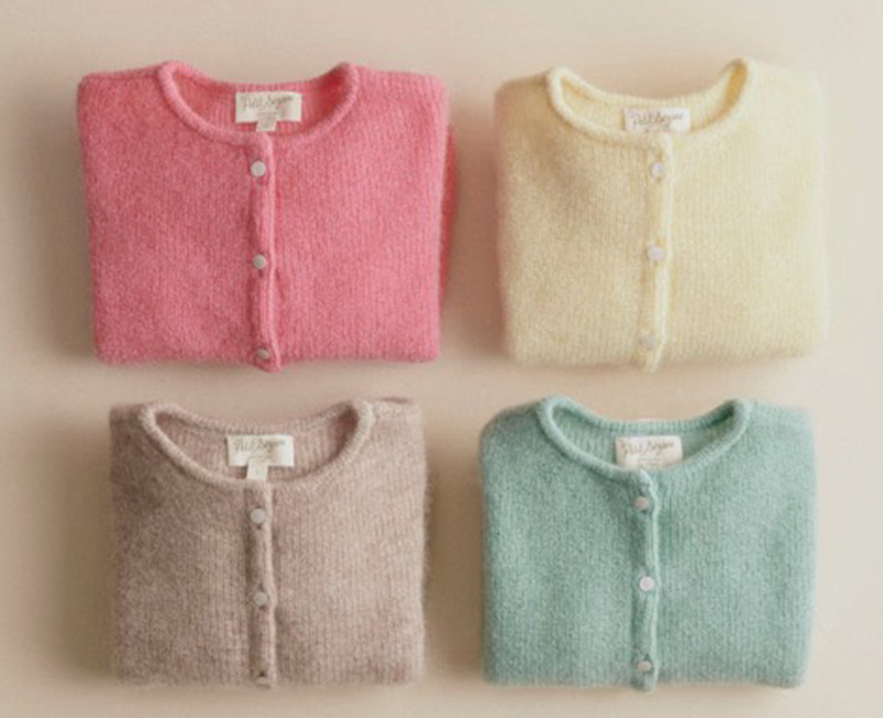 Four pastel fuzzy cardigans folded neatly in pink, cream, taupe, and mint.
