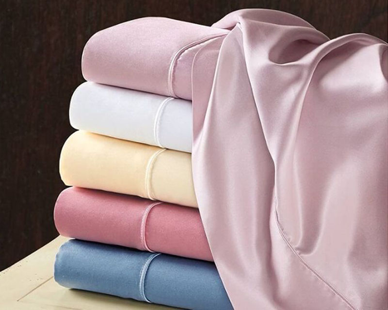 Stacked pastel folded fabrics with draped pink cloth showcasing smooth silky texture