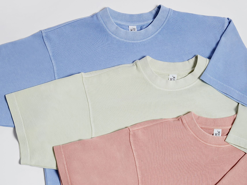 Pastel oversized T-shirts in blue, sage, and pink layered on neutral background