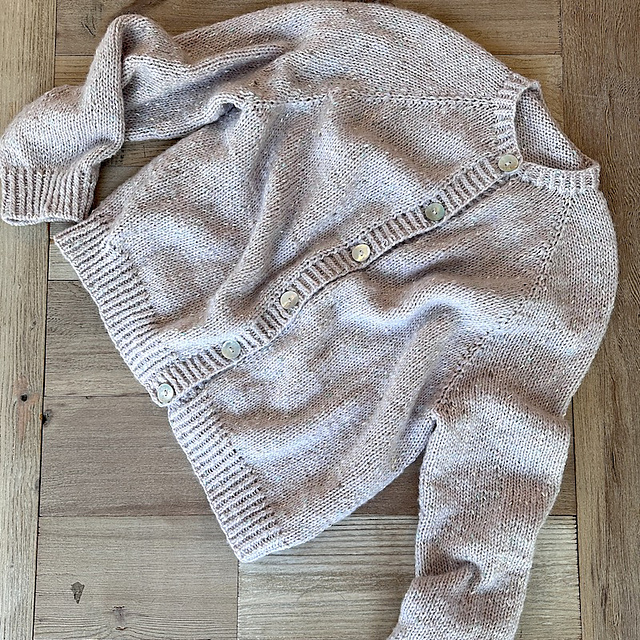Light pink knit cardigan laid flat on wooden floor with front buttons visible