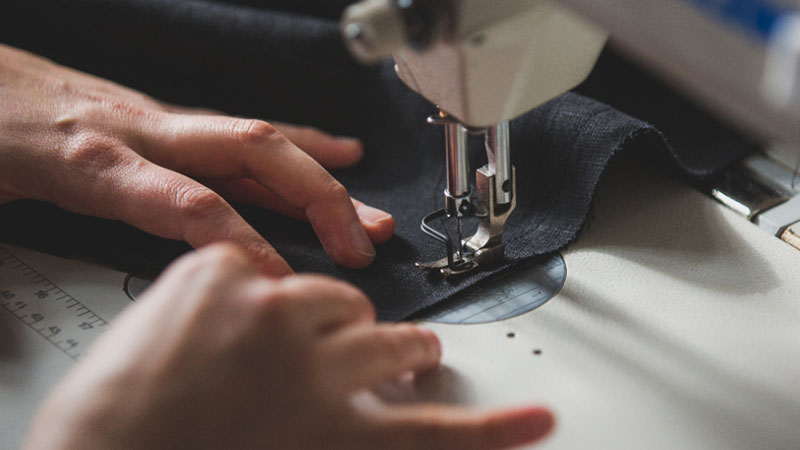 Close-up of hands guiding black fabric under the needle of a sewing machine, stitching a seam.