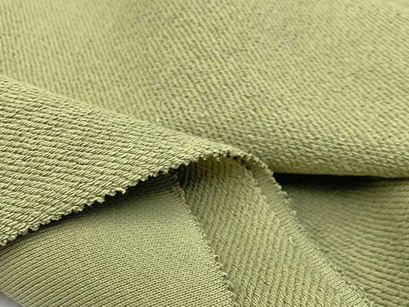 Close-up of sage green knit French Terry fabric showing textured weave and folded edge