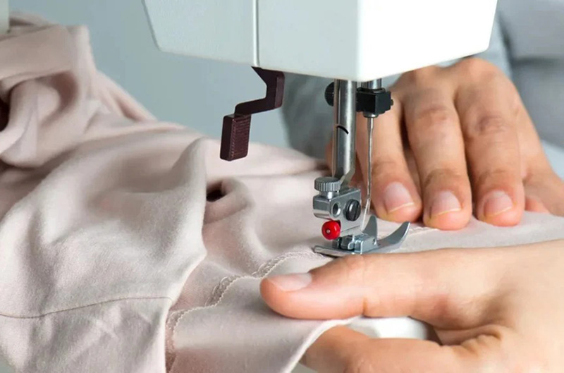 Hands guiding soft beige fabric under a sewing machine needle