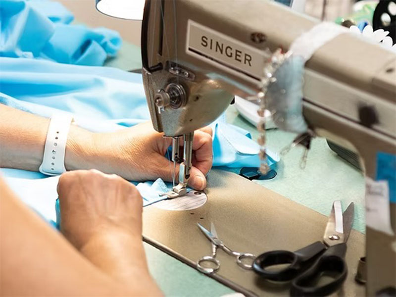 Hands guiding light blue fabric through Singer industrial sewing machine with scissors nearby