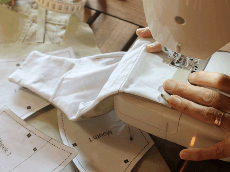 Hands sewing white fabric with machine over paper pattern pieces