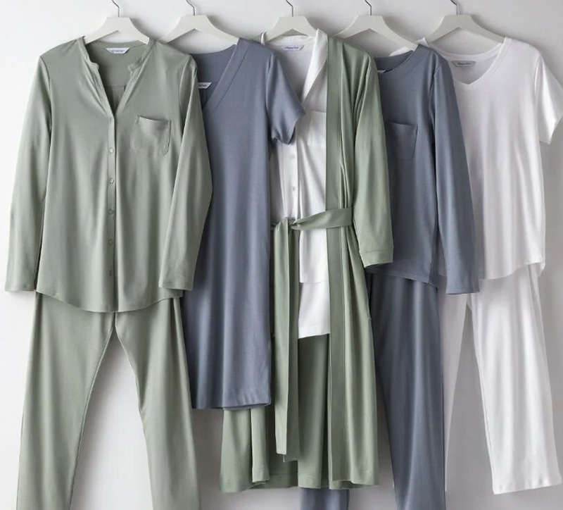 Soft pajamas set in sage, blue, and white tones hanging together on hangers.