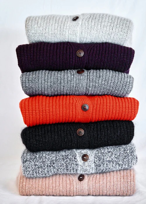 A stack of seven folded button-up cardigans in different colors