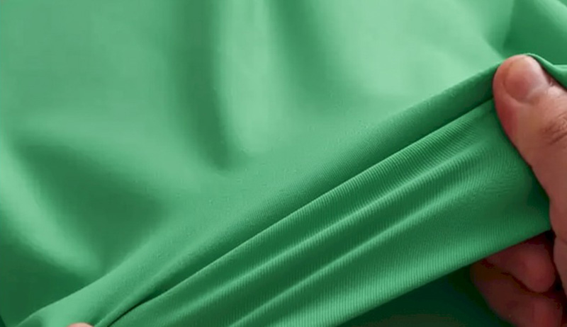 Hand stretching smooth green performance fabric to show flexibility and softness.