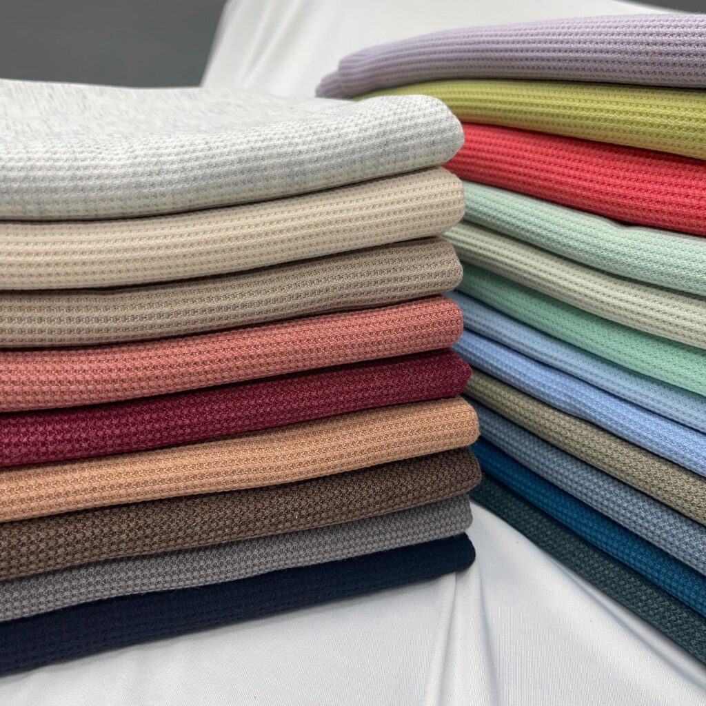 Folded waffle-knit fabrics stacked in a wide range of pastel, neutral, and deep colors.