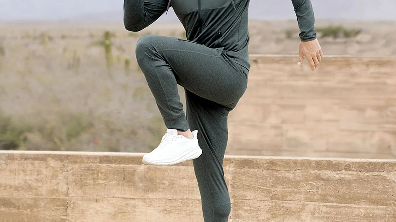 Person exercising outdoors in dark athletic leggings and white sneakers during high-knee movement.
