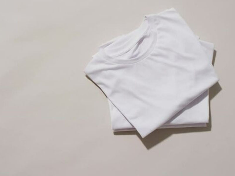 Folded white T-shirt placed on minimal light background with copy space