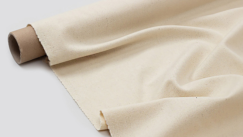 Unbleached wool fabric roll partially unfurled, showing natural texture and soft drape