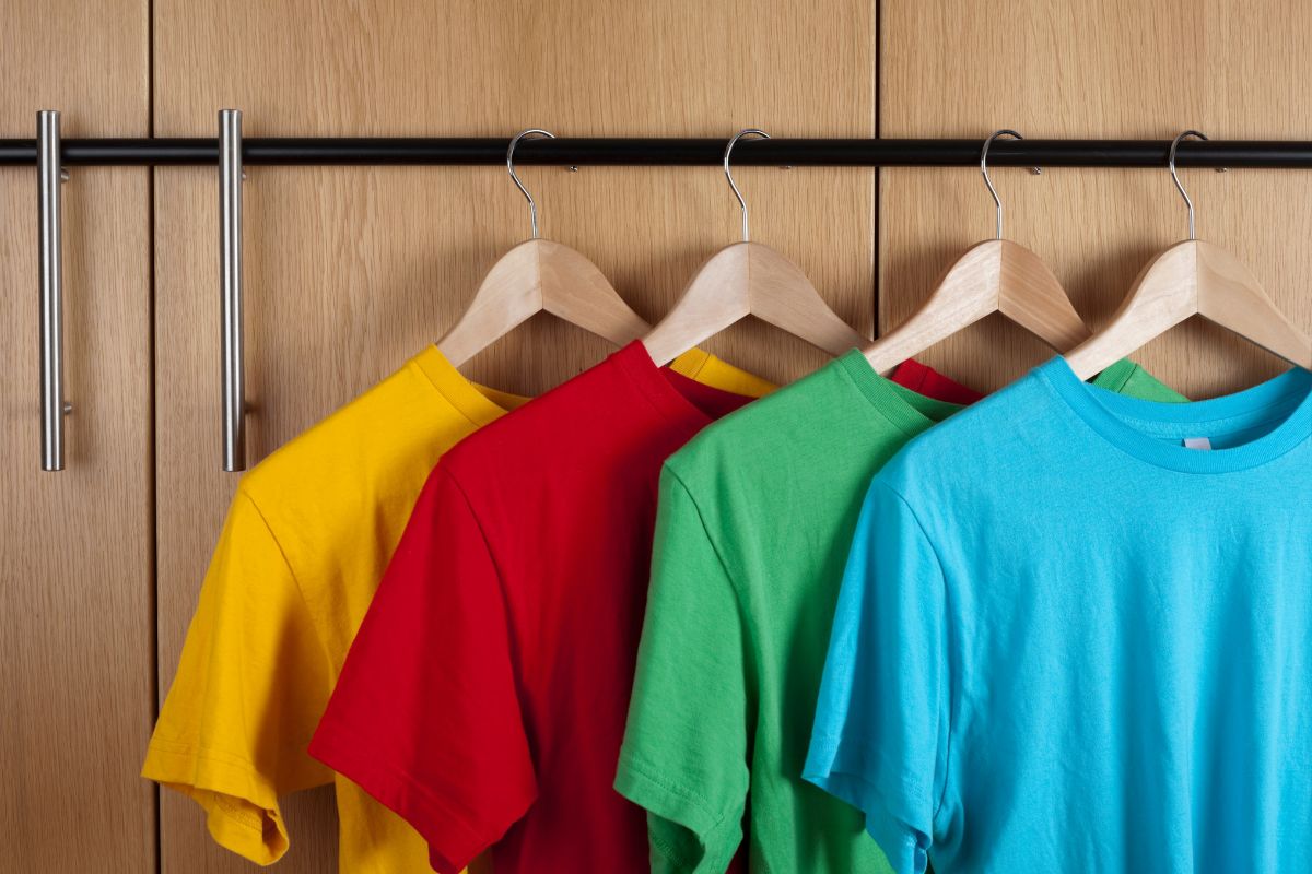 Colorful T-shirts hanging on wooden hangers against modern wardrobe doors