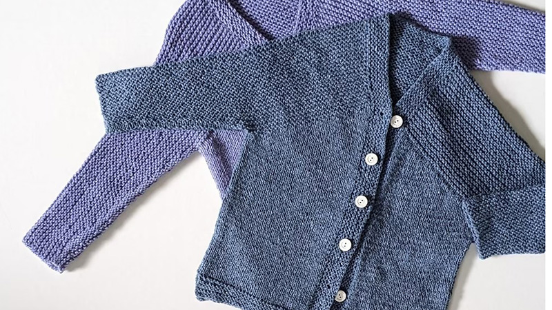 Hand-knit baby cardigans in blue and lavender layered flat with button-front detail