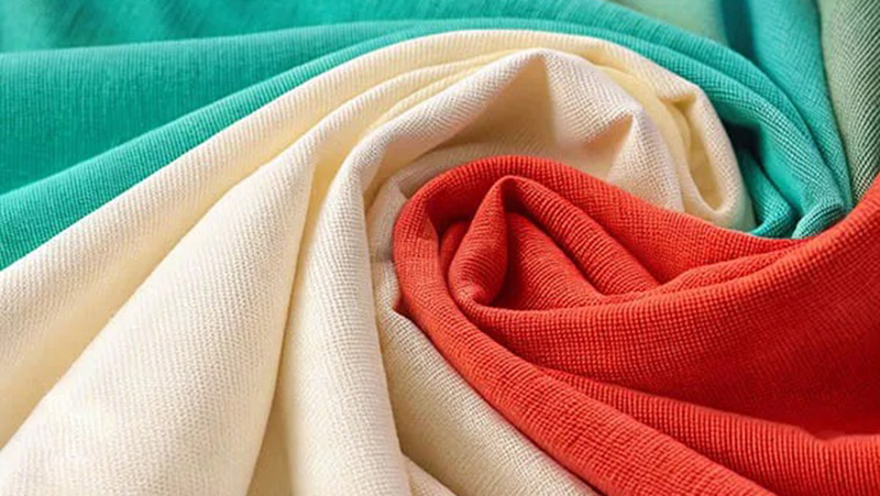 Swirled knit fabrics in turquoise, cream, and coral showing soft texture.