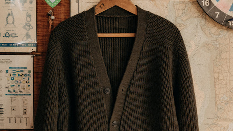 Dark ribbed knit cardigan hanging on wooden hanger against vintage wall decor